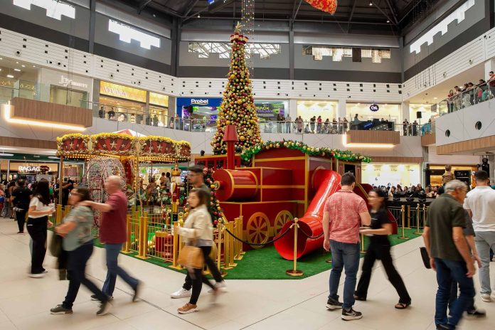 Vão central do Floripa Shopping decorado para o Natal, com grande árvore iluminada, locomotiva vermelha e carrossel, e visitantes circulando