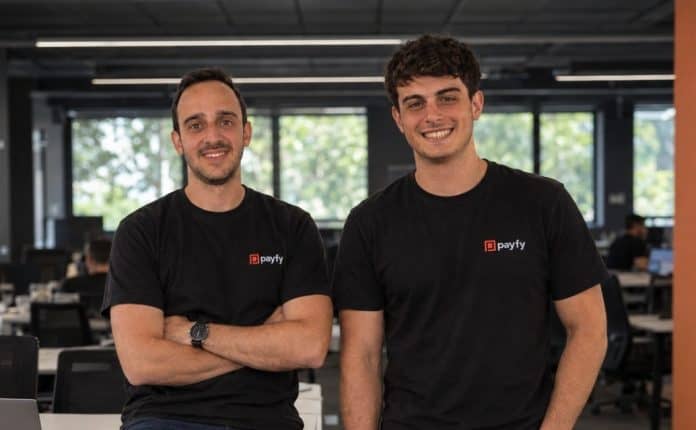 Dois integrantes da equipe da Payfy, de camiseta preta com a marca da empresa, em escritório