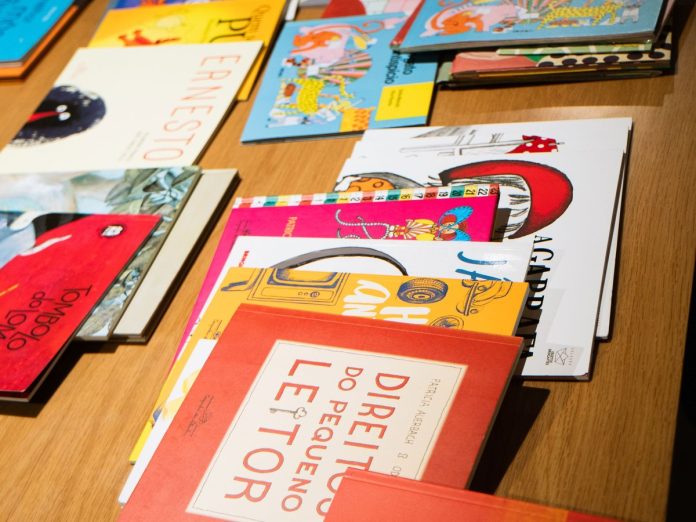 Livros infantis coloridos espalhados sobre uma mesa de madeira, entre eles Direitos do Pequeno Leitor