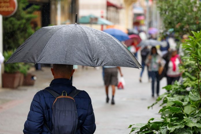 Pedestres com guarda-chuvas caminham em calçadão em dia de chuva em Santa Catarina