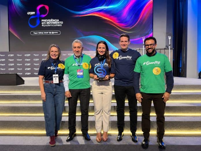 Cinco executivos da Quanta Previdência com camisetas #Quanters posam com o troféu do Selo de Engajamento Abrapp 2026 no palco do 47º CBPP