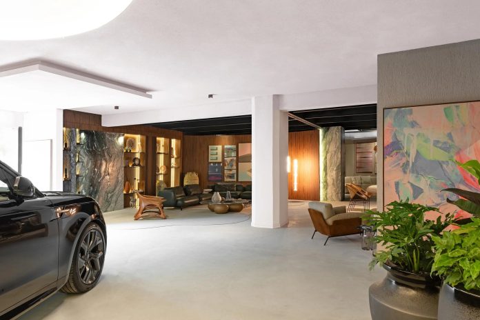 Range Rover Sport preta estacionada dentro do living Casa Acervo, com sofás escuros, estantes iluminadas e quadro colorido ao fundo