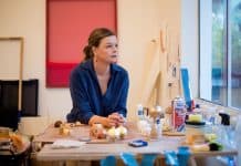 Roberta Tassinari inaugura estúdio em frente à Praça XV e lança a 3ª edição da Revista Ateliê neste sábado A artista Roberta Tassinari em seu estúdio, sentada à mesa de trabalho com materiais de pintura