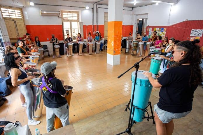 Participantes tocam timbaus em roda durante oficina do Roda de Timbau Floripa, com a professora à frente
