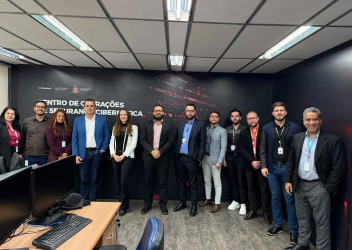 Comitiva da SCTI de Santa Catarina e equipe paulista posam diante do painel do Centro de Operações de Segurança Cibernética, em São Paulo