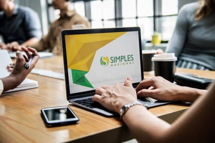 Pessoa usa notebook com logotipo do Simples Nacional na tela, em mesa de escritório