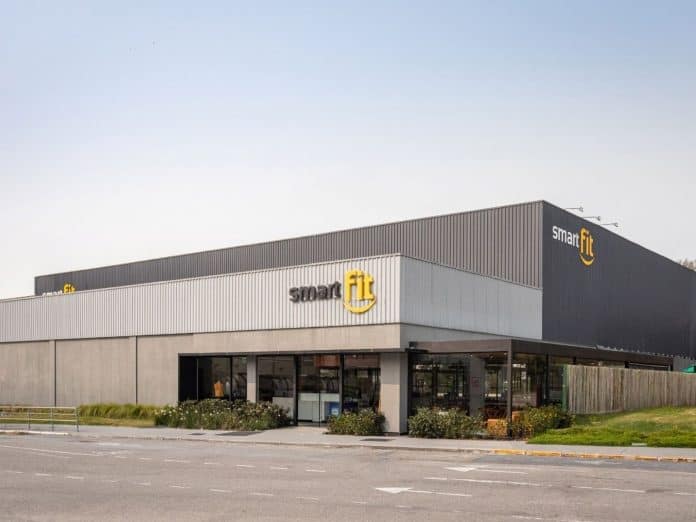 Fachada da unidade da Smart Fit no Shopping Itaguaçu, em São José, com prédio em tons de cinza e logotipos amarelos da rede