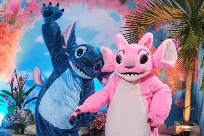 Personagens Stitch e Angel posam lado a lado em cenário tropical com flores e palmeira