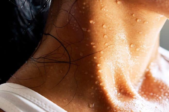 Pescoço e colo de uma mulher cobertos de gotas de suor, com regata branca