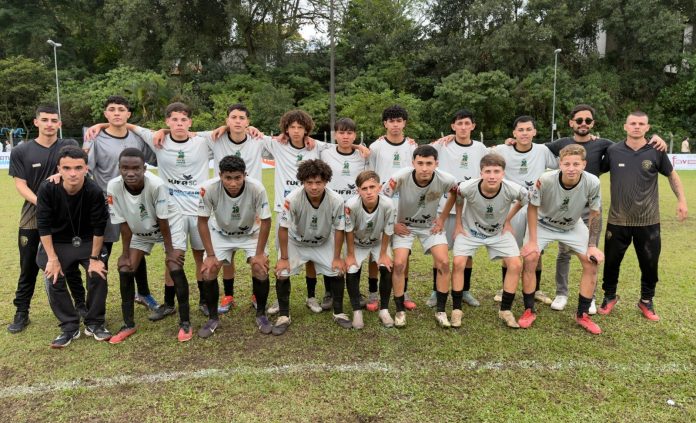 Time de jovens jogadores com uniforme branco da Taça das Favelas e da CUFA SC posa no gramado ao lado da comissão técnica
