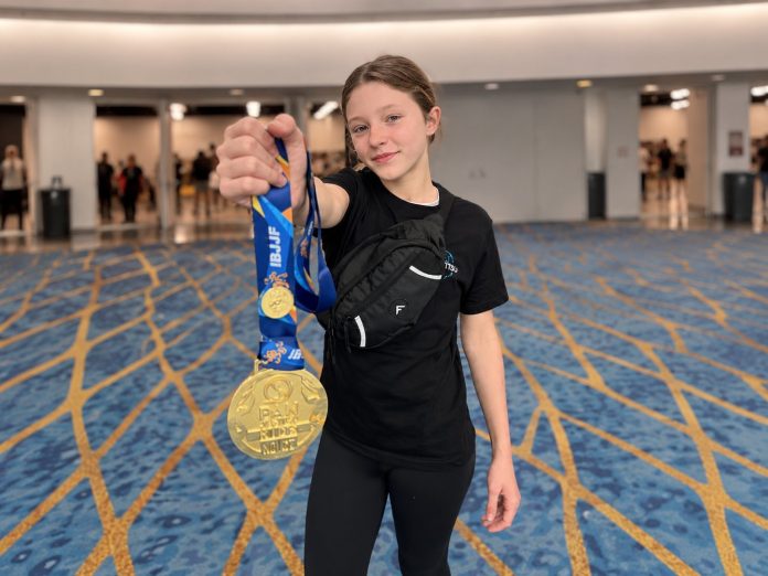 Valentina Rebellato Ferreira, de 12 anos, de camiseta preta, exibe medalhas em um salão de competição